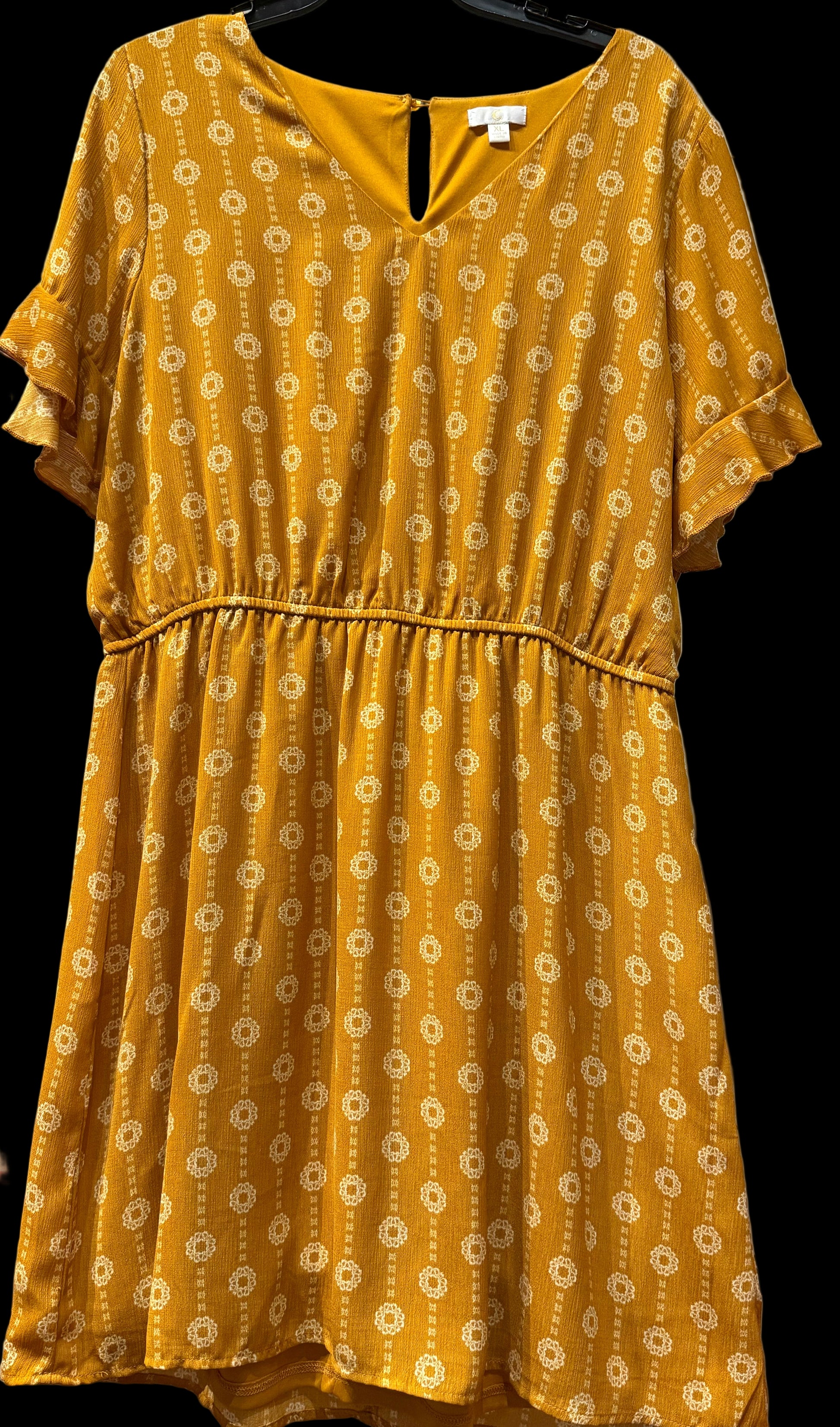 Yellow dress with a floral pattern on a hanger against a white wall.