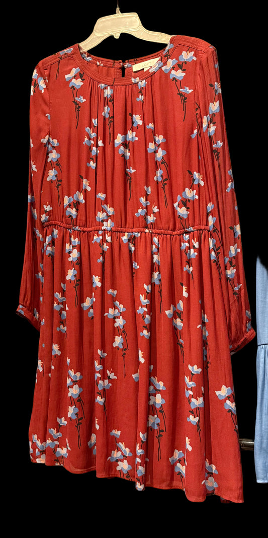 Red floral dress hanging against a brick wall.